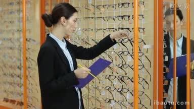 迷人的女验光师与剪贴板制作修订和计数存货可用的光学商店展示与不同的眼镜